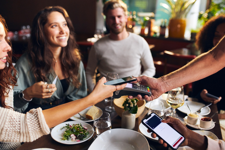 Smiling people sitting around a table at a restaurant paying contactless