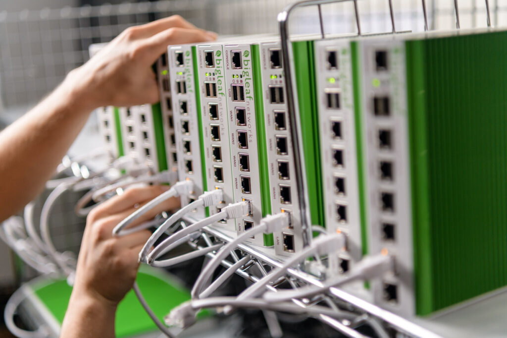 Hands connecting ethernet cables to a rack of Bigleaf Networks SD-WAN devices.